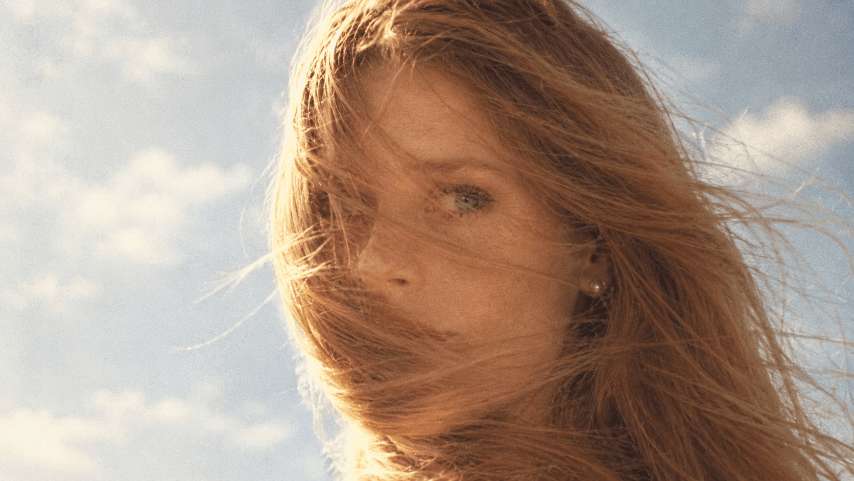Studio hero image, 2026 — a portrait in wind-blown light against a pale sky