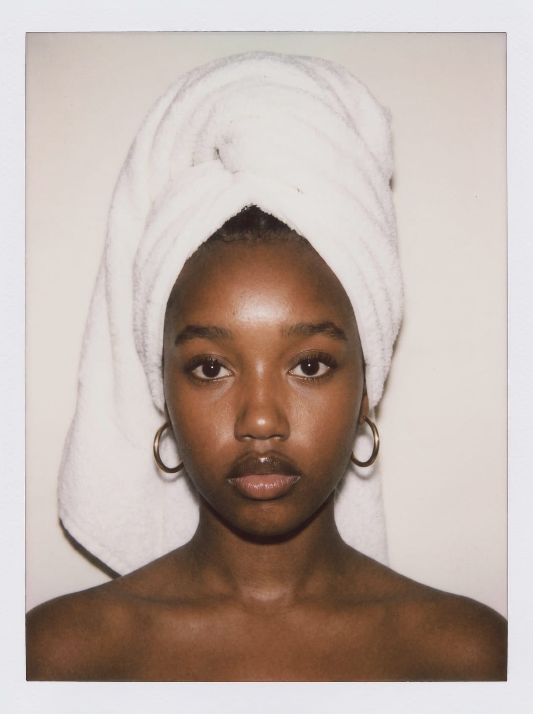 Campaign muse portrait — a model wearing a white towel wrap and gold hoop earrings, photographed in soft light