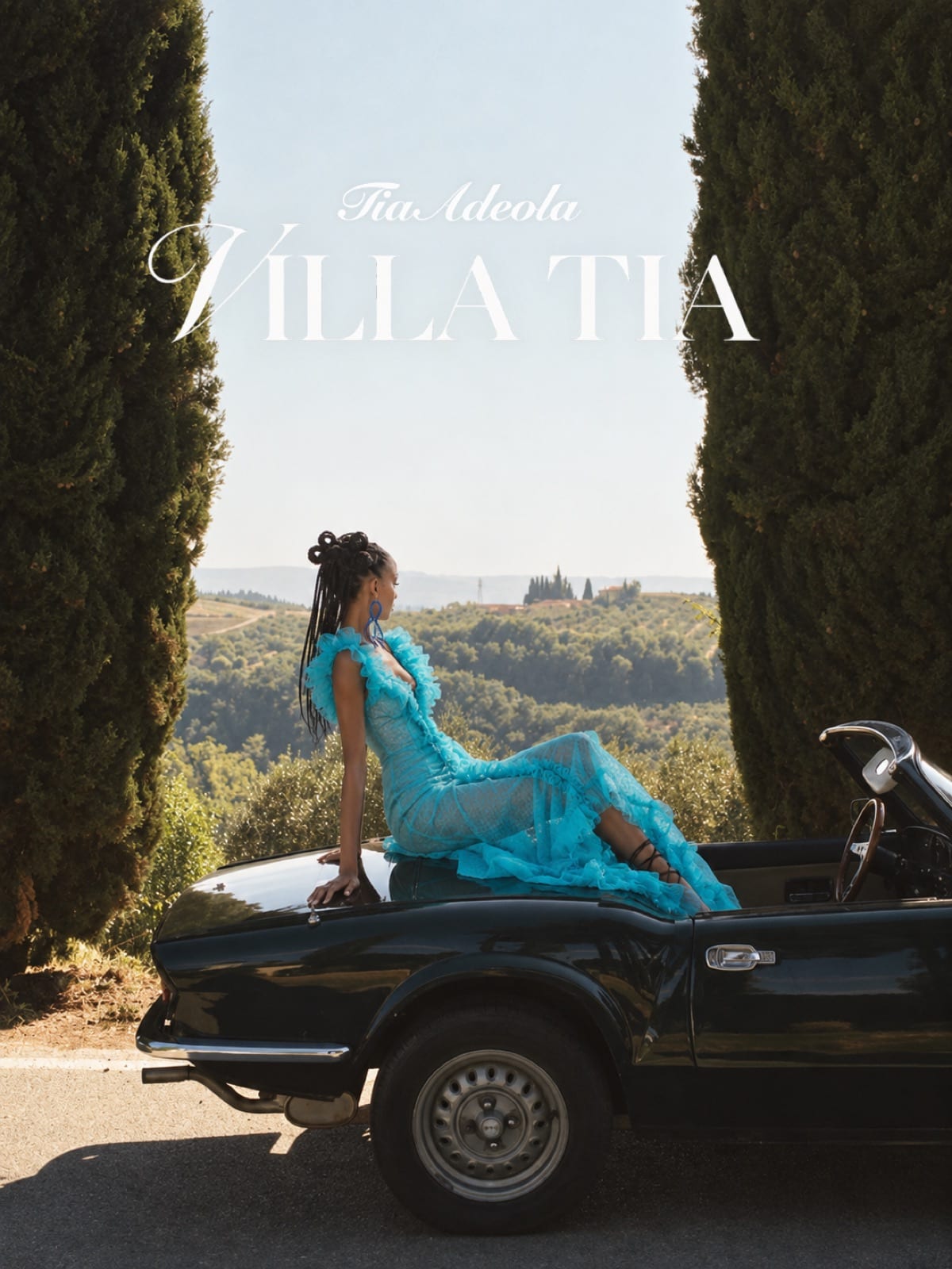 Villa Tia cover — a model in a blue ruffled gown reclining on a vintage convertible between cypress trees, with the Tia Adeola Villa Tia title