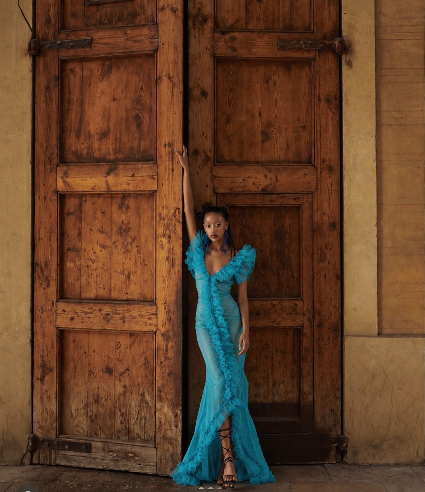 A model in the blue gown standing against weathered wooden doors, one arm raised