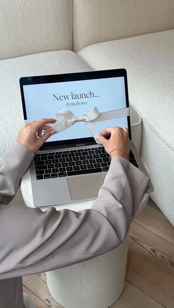 A laptop on a cream ottoman showing a New launch announcement page tied with a white ribbon