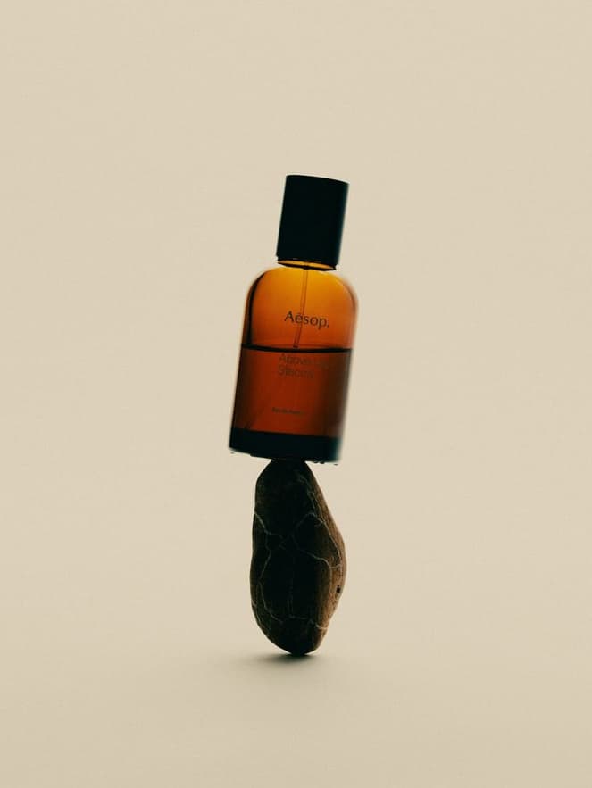 An amber Aesop bottle balanced on a dark stone against a warm beige background
