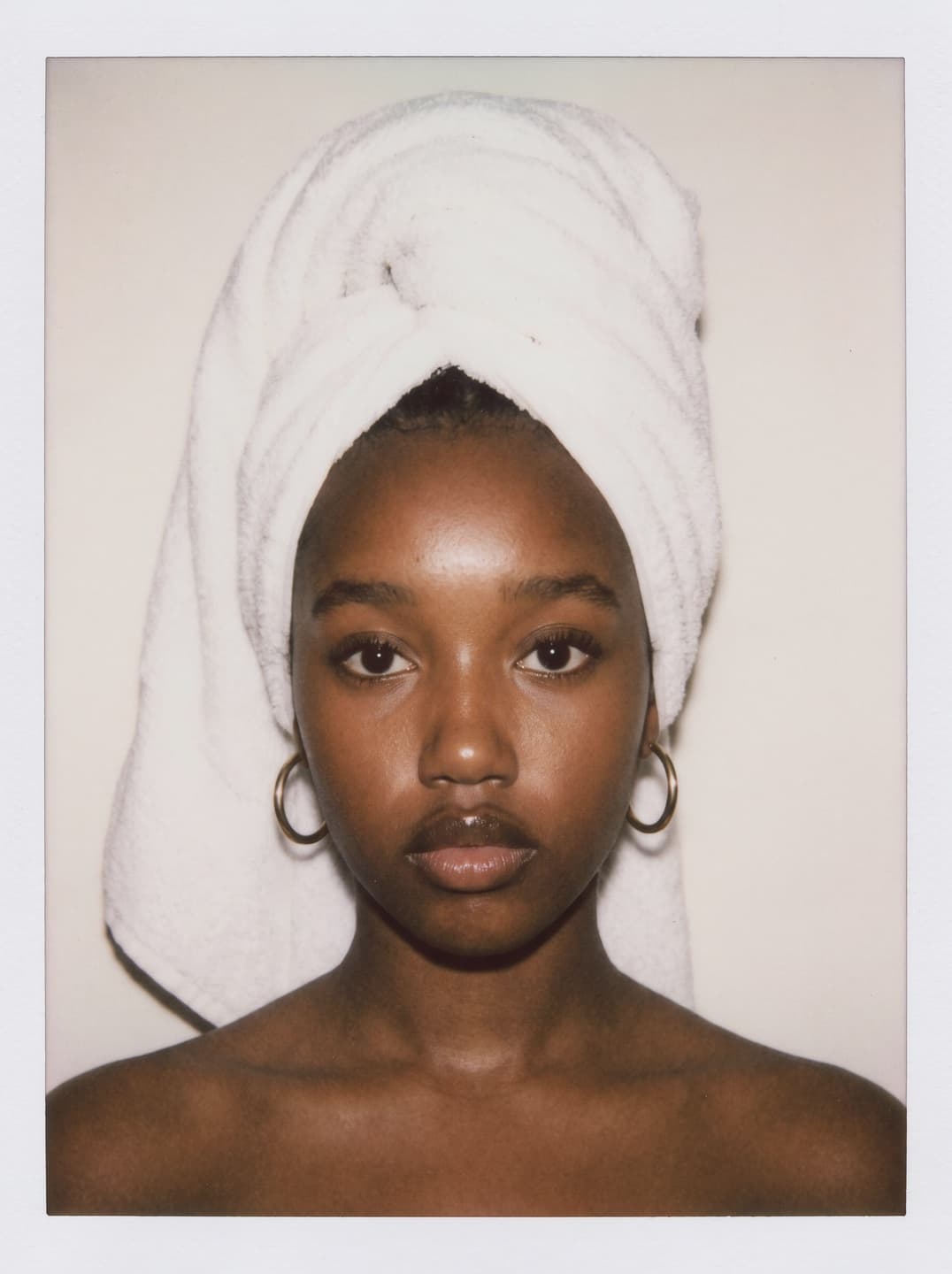 Campaign muse portrait — a model wearing a white towel wrap and gold hoop earrings, photographed in soft light